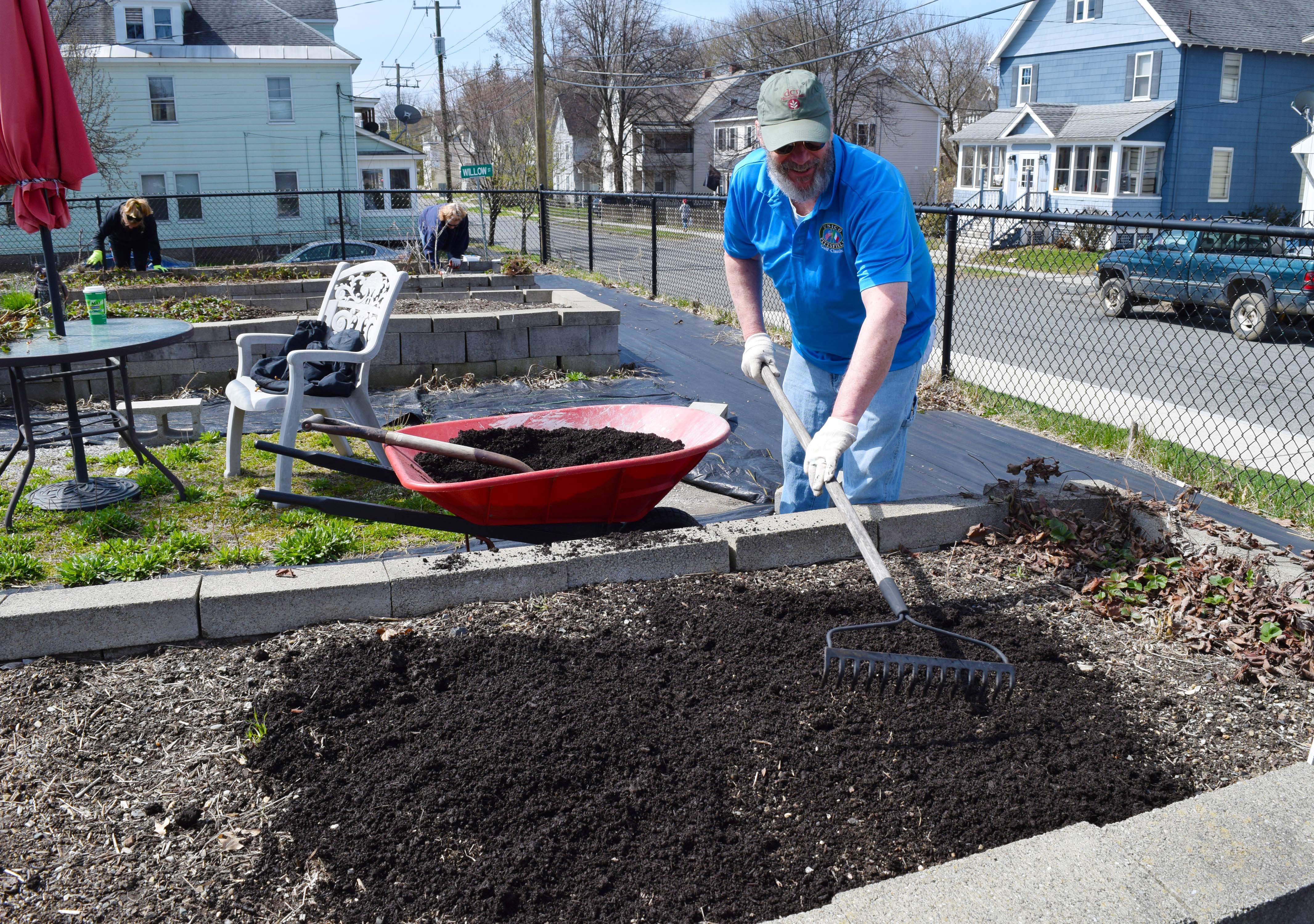 A volunteer from UNICO rakes out mulch in a garden bed