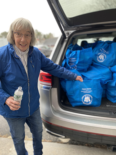 older woman points to bags of food in back of car