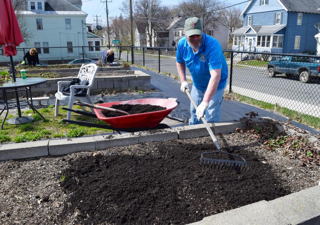 A volunteer from UNICO rakes out mulch in a garden bed