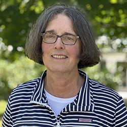 caucasian woman, short brown-gray hair, glasses, wearing blue and white striped zipper sweater
