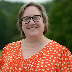 caucasian woman, short dirty blonde hair, glasses, wearing orange shirt with white dots